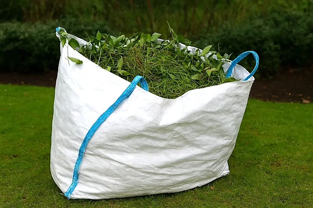 Green waste collection Perth – large white garden bag filled with grass clippings and leaves on a lawn for eco-friendly disposal.
